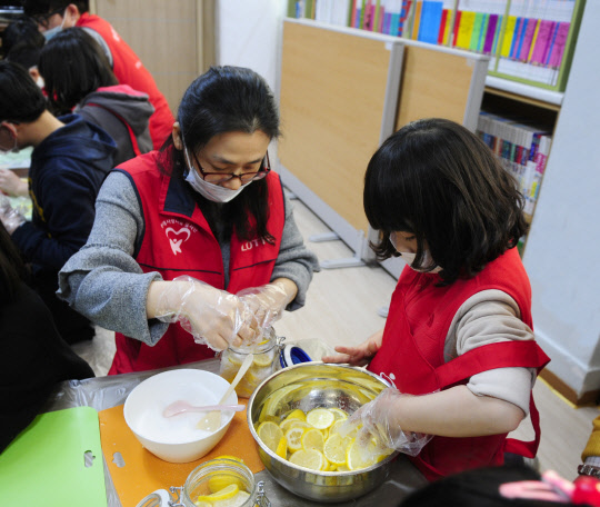 롯데정보통신 샤롯데봉사단은 지난 15일 서울 금천구 미래지역아동센터에서 아동들과 레몬청을 만들어 지역 노인복지관에 기부하는 사회봉사활동을 했다고 16일 밝혔다. 봉사단원과 어린이가 레모청을 만들고 있다.  롯데정보통신 제공